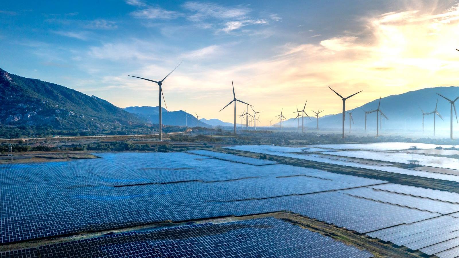 Weitläufige Photovoltaikanlage und Windräder in einer Talebene im Morgenlicht